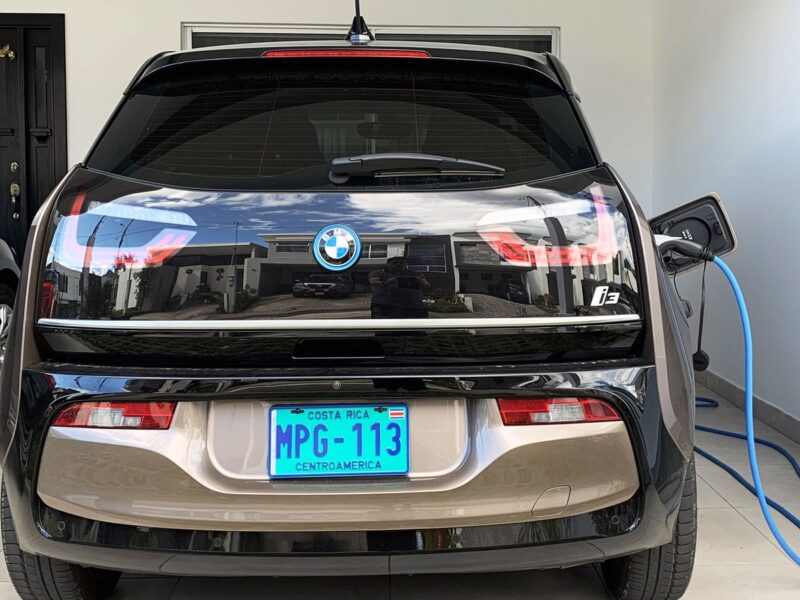 A BMW i3 electric car charging from a wall-mounted charger in a home garage