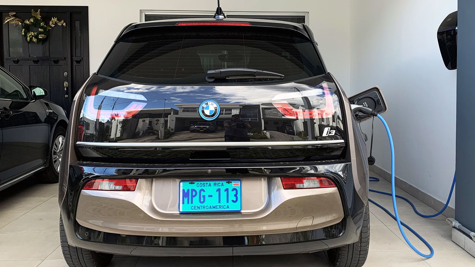 A BMW i3 electric car charging from a wall-mounted charger in a home garage