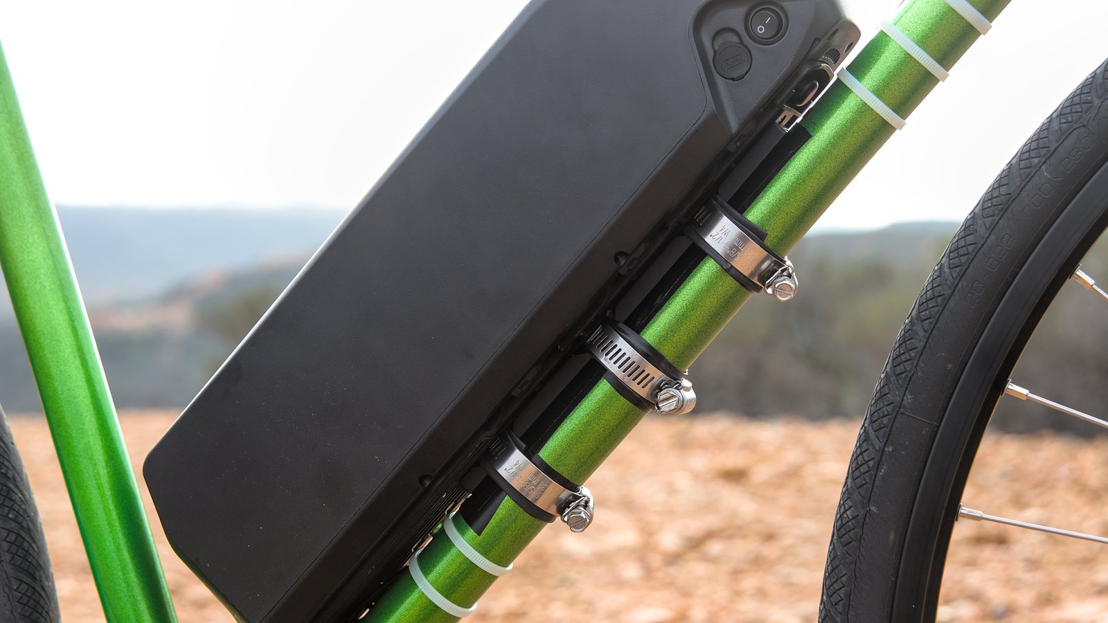 A black e-bike battery pack fixed to the green frame of a bicycle