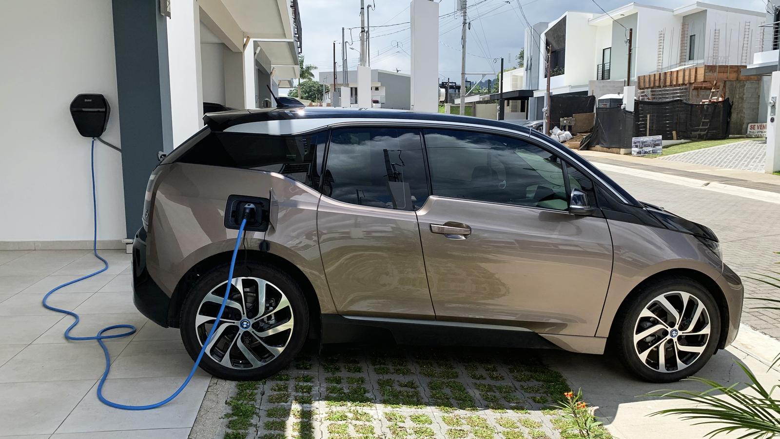 An electric car charging on a home driveway from a wall-mounted charger