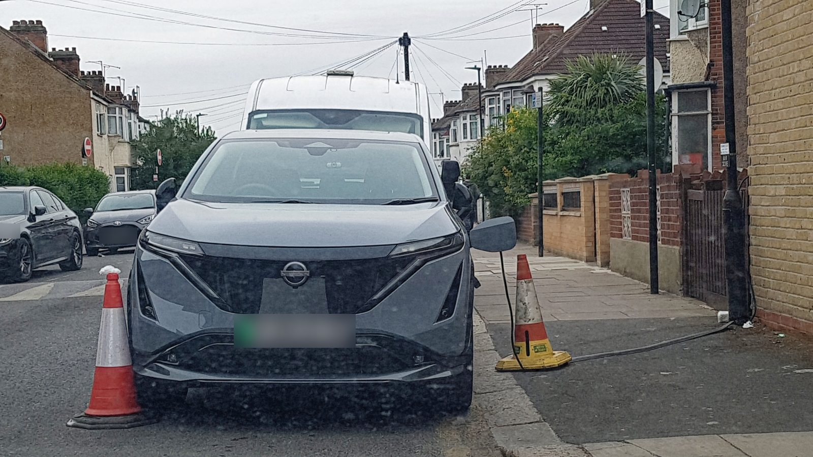 A charging cable trailed across a pavement to a grey electric car parked on a residential street in Haringey, London.