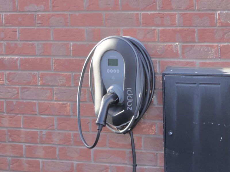 A wall-mounted home electric car charger with a tethered cable on an outside brick wall