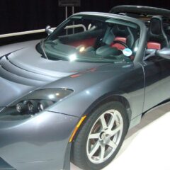 The original Tesla Roadster, a grey two-seat electric sports car, on display at a motor show