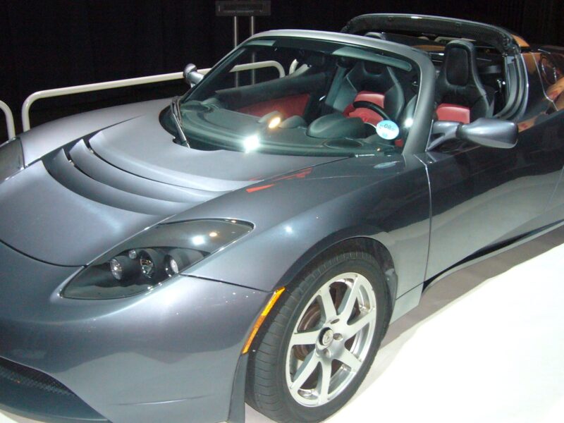 The original Tesla Roadster, a grey two-seat electric sports car, on display at a motor show