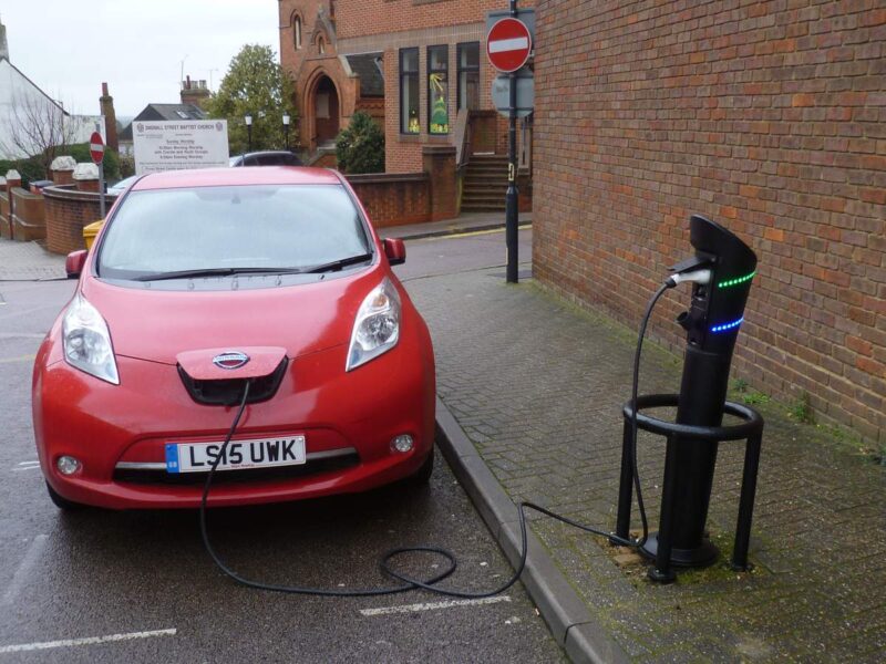 A red Nissan Leaf parked at the kerb and plugged into an on-street charging post in St Albans