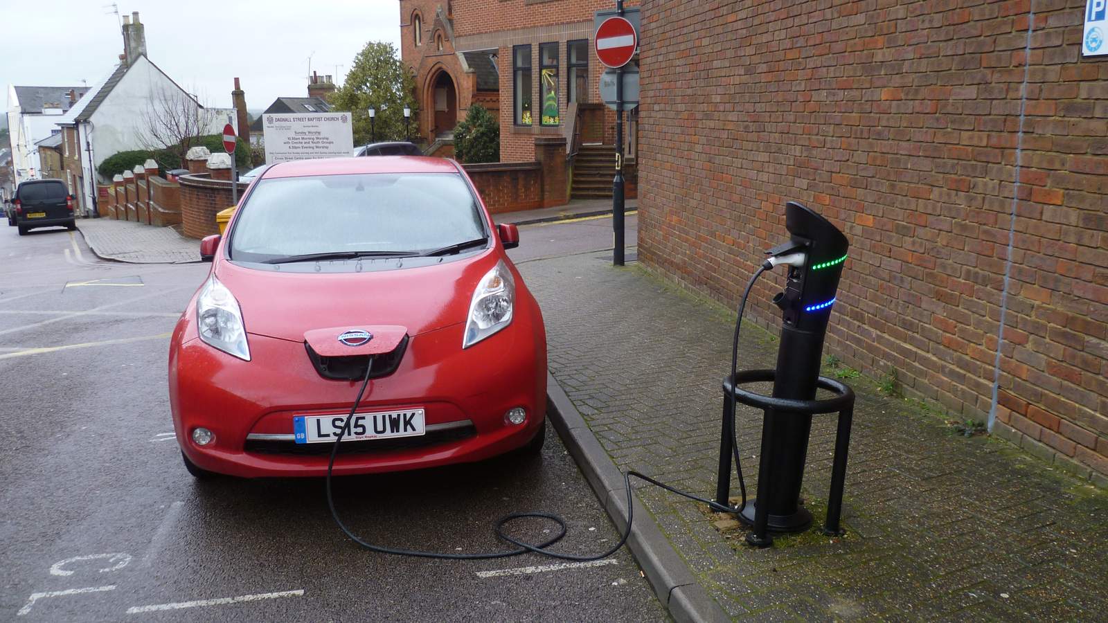 A red Nissan Leaf parked at the kerb and plugged into an on-street charging post in St Albans