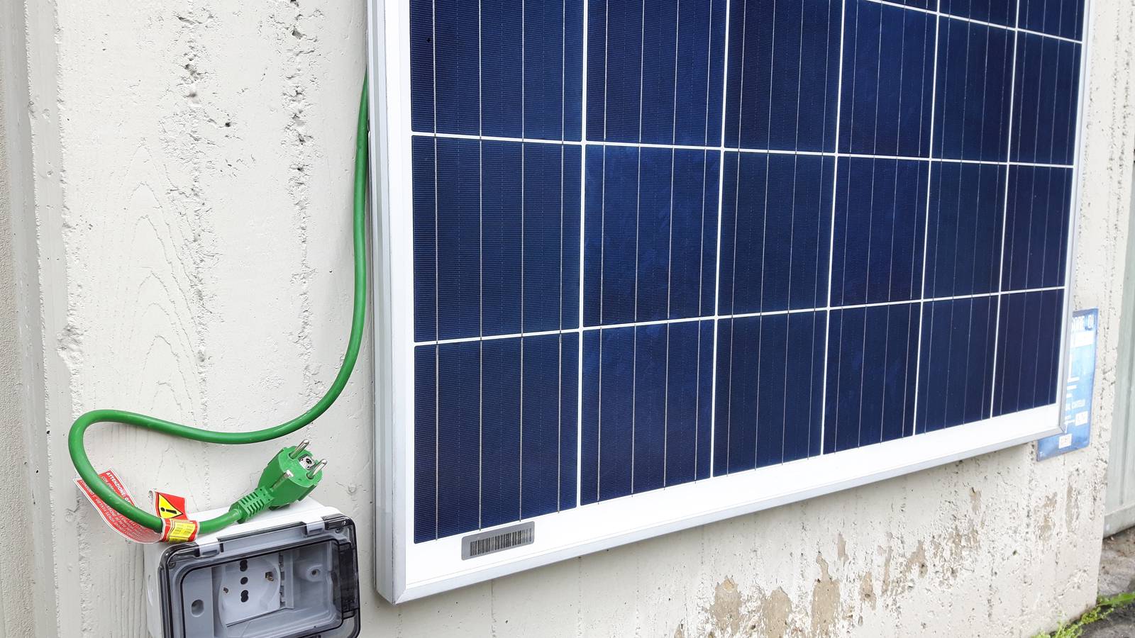 A small plug-and-play solar panel fixed to an outside wall, with its cable running to a weatherproof socket