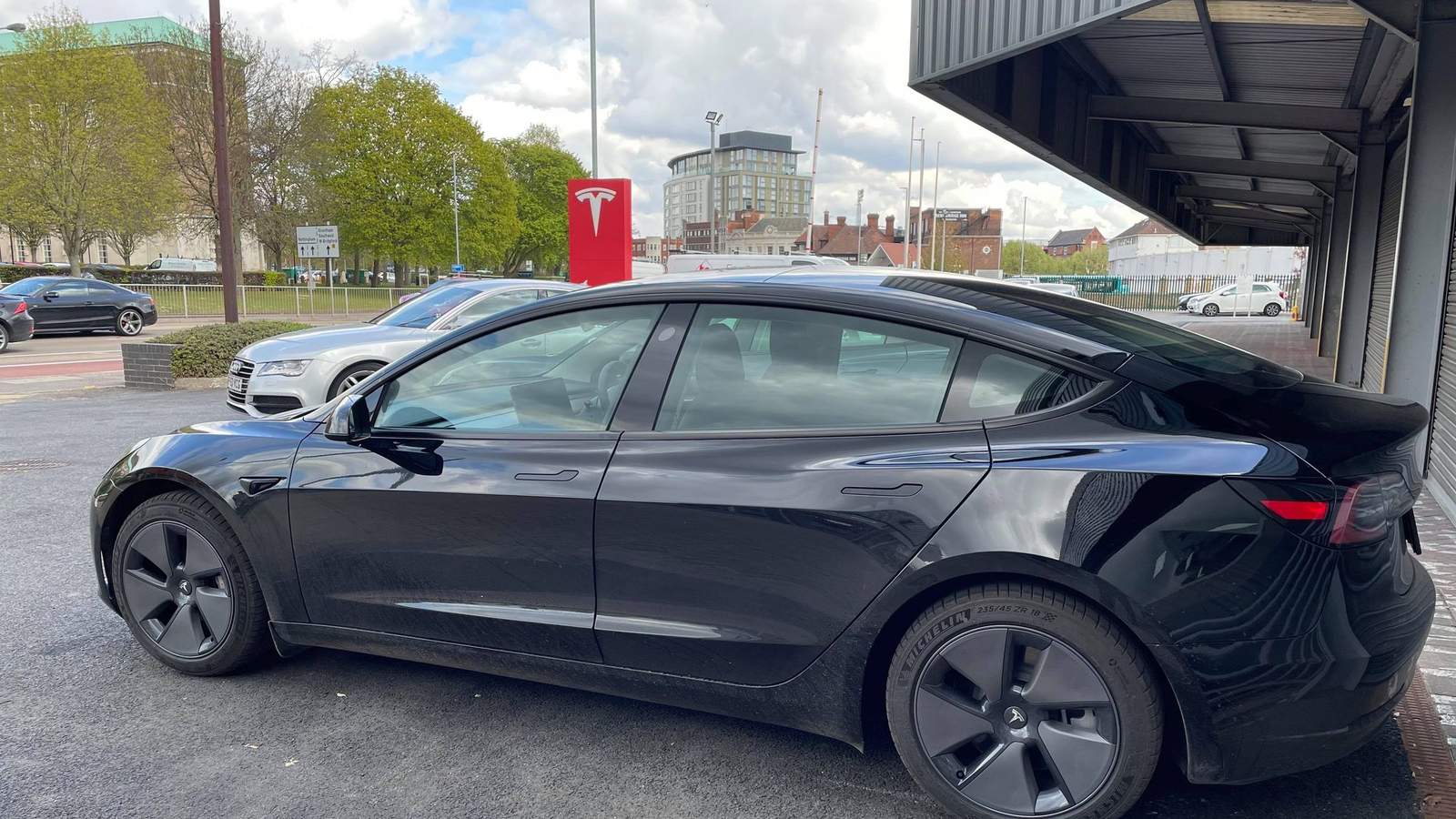 A black Tesla Model 3 electric car parked in front of a Tesla sign in Nottingham