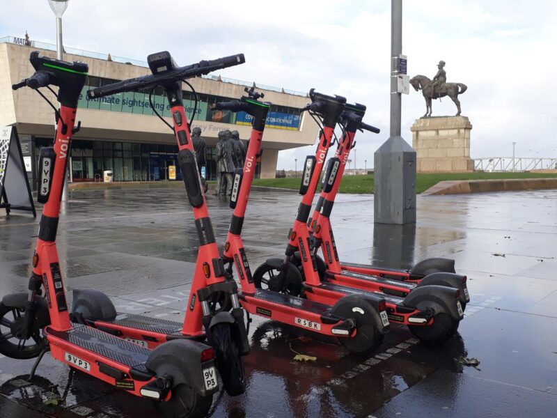 Red Voi rental e-scooters parked together on a paved area in Liverpool